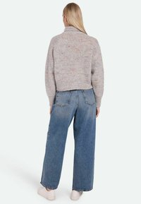 Gray knitted sweater with a high collar, textured finish, paired with loose-fitting blue jeans and white sneakers.