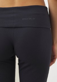 Mørk navy ribbe leggings med en bred, glatt midjebånd preget med "ONLY PLAY." Tøyet ser ut til å være elastisk og tettsittende.