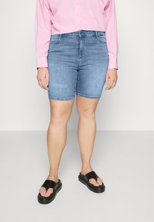 Jeanshorts i lyseblå, knelengde, med et klassisk femlommersdesign. Kombinert med en rosa skjorte med knapper og svarte sandaler.
