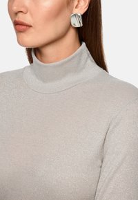 Hellgrauer, gerippter Rollkragenpullover mit weicher Textur, kombiniert mit einem glänzenden, unregelmäßig geformten silbernen Ohrring.