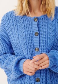 Blå stickad cardigan med ett texturerat mönster, featuring mörka knappar, ribbade ärmslut och en lös passform.