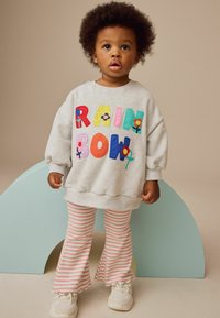 Grauer Pullover mit bunten, gestickten Buchstaben, die "RAINBOW" buchstabieren, und floralen Akzenten, kombiniert mit rosa und weißen gestreiften Schlaghosen.