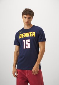 Jūras spēku kokvilnas t-krekls ar "DENVER" dzeltenā un baltā krāsā; ar spēlētāja numuru 15, pabeigts ar Nike logo dzeltenā krāsā uz pleca.