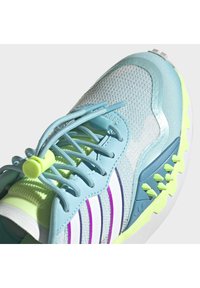 Light blue athletic shoe featuring a mesh upper, elastic laces with a green toggle, white and purple stripes, and textured rubber outsole accents.