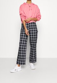 Różowa bluza z kapturem z kieszenią z przodu, czarno-białe spodnie o szerokich nogawkach w kratę oraz białe trampki. Nowoczesny design z luźnym krojem.