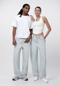 Light blue wide-leg jeans paired with a white t-shirt and tank top. Individuals have varying textures in hair and wear casual sneakers.