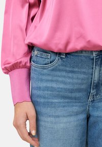 Blouse en satin rose avec manches bouffantes et poignets festonnés, associée à un jean en denim bleu clair avec un design classique à 5 poches et des effets froissés.