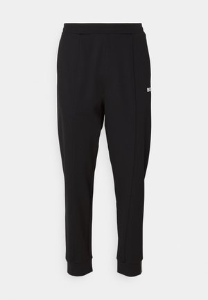 Svarte joggebukser lavet af blødt stof, med en tætsiddende pasform, elastisk talje, ribbede manchetter og et lille hvidt logo på siden.