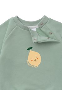 Minzgrüner Sweatshirt mit weicher Textur. Enthält eine gelbe Zitronen-Grafik mit einem Lächeln und dem Text "Nutze den Tag." Druckknopfverschluss am Ausschnitt.