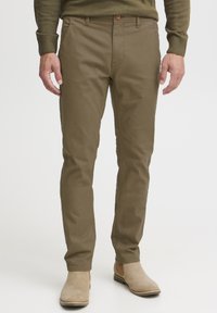 Chinos caqui con un diseño ajustado, confeccionados en una suave tela de algodón, con cierre de botón y lazos para cinturón. Llevados con botas de tobillo en color beige claro.