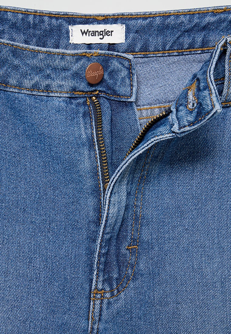 Niebieskie dżinsy z zamkiem błyskawicznym, z brązowym metalowym guzikiem i żółtym przeszyciem. Widoczna metka Wrangler na pasku.