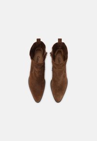 Bottines en daim marron, à bout pointu, talon bas et fermeture éclair, avec une texture douce et une boucle à l'arrière pour un enfilage facile.