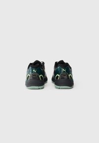Et par sorte og grønne Puma sneakers set fra bagved, der viser hælen, sålmønsteret og brandlogoet på hver sko.