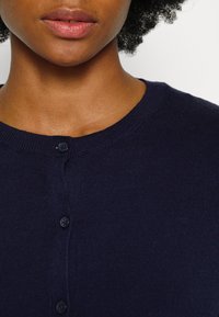 Marinblå cardigan med rund halsringning, ribbat mönster och fem mörka knappar framtill, som visar upp en komfortabel stickad finish.