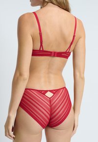 Ensemble de lingerie en dentelle rouge comprenant un soutien-gorge à lanières et une culotte taille haute assortie avec un motif en chevrons et un détail en trou de serrure à l'arrière.