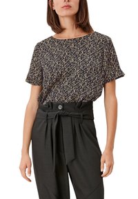 Top nero a maniche corte con un motivo astratto dorato, colletto tondo, abbinato a pantaloni neri a vita alta con cintura annodata e dettaglio a bottone.