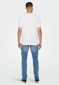 White short-sleeve t-shirt with a round neckline, paired with light blue denim jeans. The outfit features casual black sneakers.