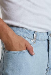 Jeans de mezclilla azul claro con un ajuste clásico, que presentan una cremallera plateada, un cierre de botón y un bolsillo frontal con detalles de costura visibles.