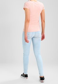 Camiseta ajustada de color rosa claro y vaqueros skinny de color azul claro. La camiseta tiene mangas cortas; los vaqueros tienen una textura suave con un ligero desgaste. Zapatillas negras.