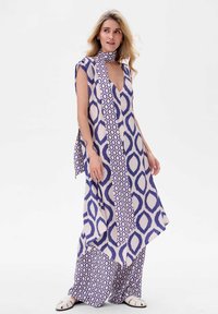 Wielokolorowa sukienka maxi z głębokim dekoltem w kształcie litery V, zdobiona geometricznym wzorem w kolorze fioletowym i kremowym. Gładki materiał, zwężający się krój i bezrękawowy fason.