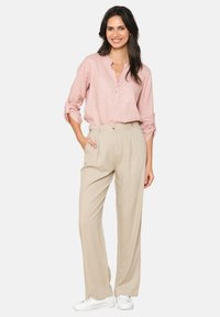 Light pink button-up shirt with a collar and pocket, paired with beige, wide-leg trousers and white sneakers. Smooth fabric texture.