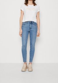 Camiseta de manga corta gris claro con"vacay" en naranja claro, combinada con jeans azules ajustados y mocasines de plataforma beige.