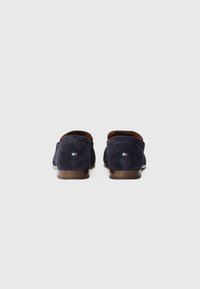 Marineblaue Wildleder-Loafer mit einer braunen Sohle, die ein kleines, dreifarbigen Logo an der Ferse aufweisen und ein glattes, minimalistisches Design haben.
