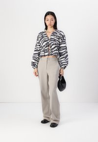 Blusa cropped preta e branca com padrão de zebra e mangas longas bufantes, combinada com calças largas cinza claro e mala preta.