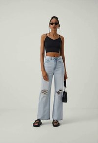 Juodas trumpas tankų palaidinė su iškirptėmis, šviesiai mėlynos plačios kelnės su skylėmis, juoda rankinė ir juodi platforminiai sandalai.