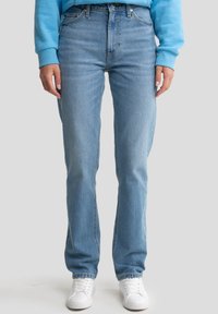 Jeans de mezclilla azul claro con una cintura alta, piernas rectas y una sutil textura descolorida, combinados con zapatillas blancas y un sudadera azul.