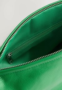 Innenraum einer grünen Lederhandtasche mit glatter Textur, ausgestattet mit einem silbernen Reißverschluss und einem zusätzlichen Reißverschlussfach zur Organisation.