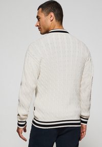 Suéter de punto trenzado en color crema con un ribete en negro y blanco en el cuello y los puños, y un patrón texturizado en toda su superficie.