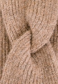 Beige gebreid sweaterstof met een gedraaide design, die een textuurpatroon toont met zichtbare vezels en een zachte afwerking.