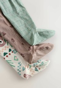 Trois paires de chaussettes pour enfants à motifs : quadrillage vert, marron avec des impressions d'ours, et blanc avec des formes géométriques. Toutes ont des semelles en caoutchouc texturé.
