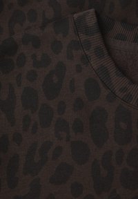 Tissu en imprimé léopard noir avec un fond brun riche, présentant une texture douce et des détails côtelés au niveau du col.