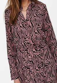 Abito camicia con stampa animale rosa e nera, con chiusura a bottoni, colletto, maniche lunghe e vita legata per dare forma e dettaglio.