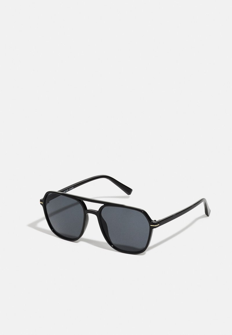 Schwarze Sonnenbrille mit achteckigem Rahmen, dunklen Gläsern, glänzender Oberfläche, dünnen Bügeln und goldenen Akzenten auf der Vorderseite.