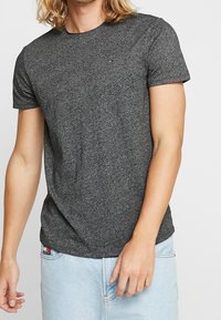 Dark gray short-sleeve t-shirt in a blended fabric, featuring a crew neck and a small logo on the chest, worn with light blue jeans.