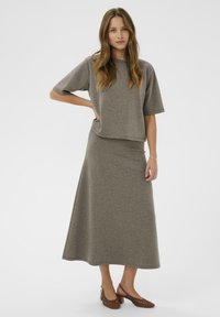 Harmaa, lyhythihainen paita yhdistettynä vastaavaan pitkään hameeseen, joka on valmistettu pehmeästä, tekstuurista kankaasta. Ruskeat, kudotut korkokengät täydentävät asua.