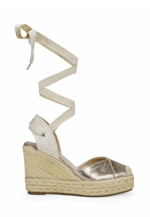 Sandal de cuña de esparto metálico plateado con suela de yute texturizada, un tacón trenzado y largas cintas de tela beige para los tobillos. Diseño de puntera abierta.