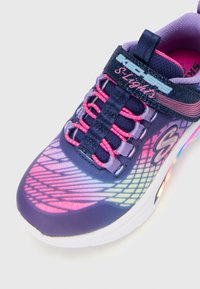 Sneaker Skechers S Lights di colore viola con lacci rosa e bianchi, rete glitterata, suola luminescente e chiusura con strap in Velcro.