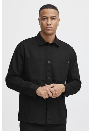 Black long-sleeve shirt with a collar, two chest pockets, and button closure. Made of smooth fabric, featuring a straight cut and minimal design.