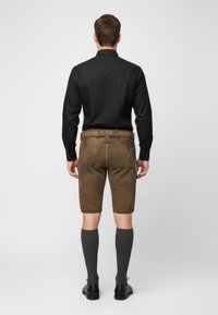 Pantalones cortos de cuero marrón con un acabado texturizado, combinados con una camiseta de manga larga negra, calcetas grises hasta la rodilla y zapatos negros, vistos desde atrás.