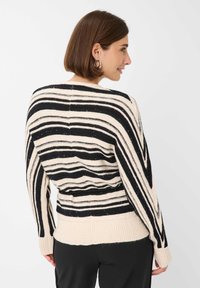 Schwarz und creme gestreifter, oversized Pullover mit geripptem Saum, der aus strukturiertem Strick und subtilen Glitzerdetails besteht. Rückansicht gezeigt.