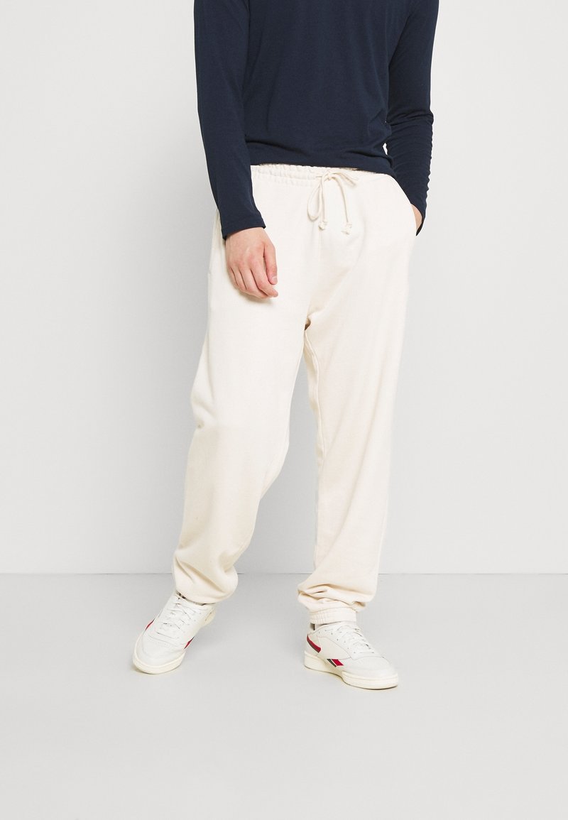 Beige bomullsbyxor med resårmidja och dragsko, med en lös passform och avslutade benslut. Matchas med vita sneakers.