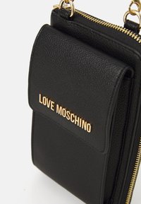 Schwarze Lederhandtasche mit texturiertem Oberflächen, ausgestattet mit einem goldfarbenen "LOVE MOSCHINO"-Logo, Reißverschluss und schlankem Design für einfache Tragbarkeit.