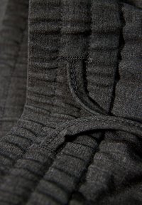 Svart tyg med en mjuk, texturerad yta. Har en sydd söm och en rynkad elastisk midja för flexibilitet och komfort.