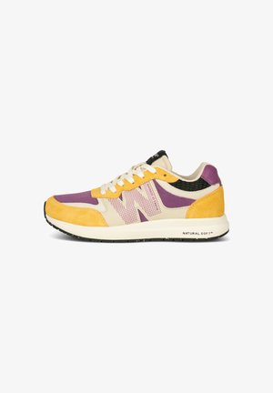 Sneaker mit einer lila Mesh-Oberfläche, gelben Wildleder-Akzenten und einer schwarzen strukturierten Ferse. Verfügt über eine weiße Zwischensohle, die "NATURAL SOFT" beschriftet ist.