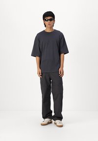 Mørkegrå oversized t-shirt, løse cargobukser og hvide sneakers med beige detaljer. Tilbehør inkluderer sorte solbriller. Enkel design.