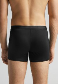 Boxers en coton noirs avec une coupe ajustée et une ceinture élastique douce, affichant un design minimal avec aucun motif ni élément visible.